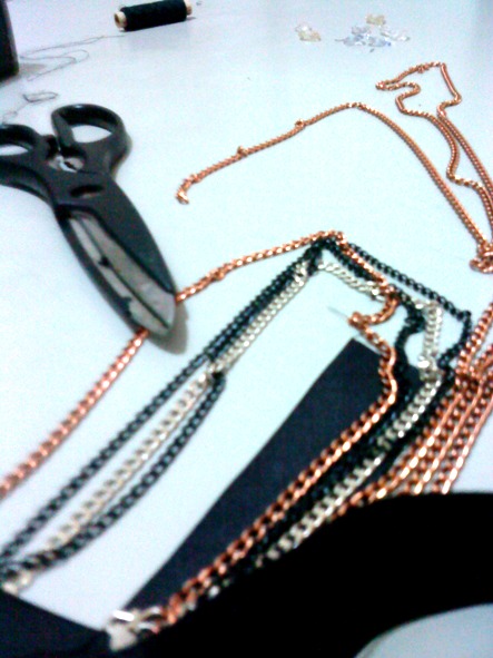 some bronze, silver and black chains with black ribbon and a pair of scissor